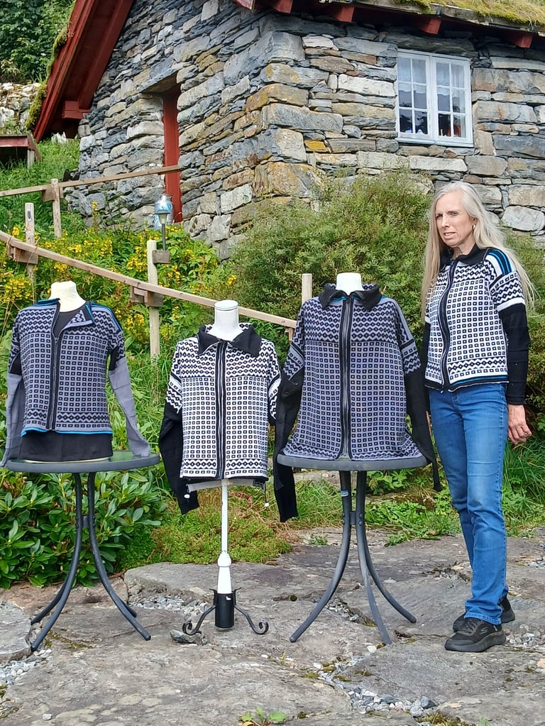 Woman standing next to mannequins wearing navy and white patterned cardigans outside a stone cottage